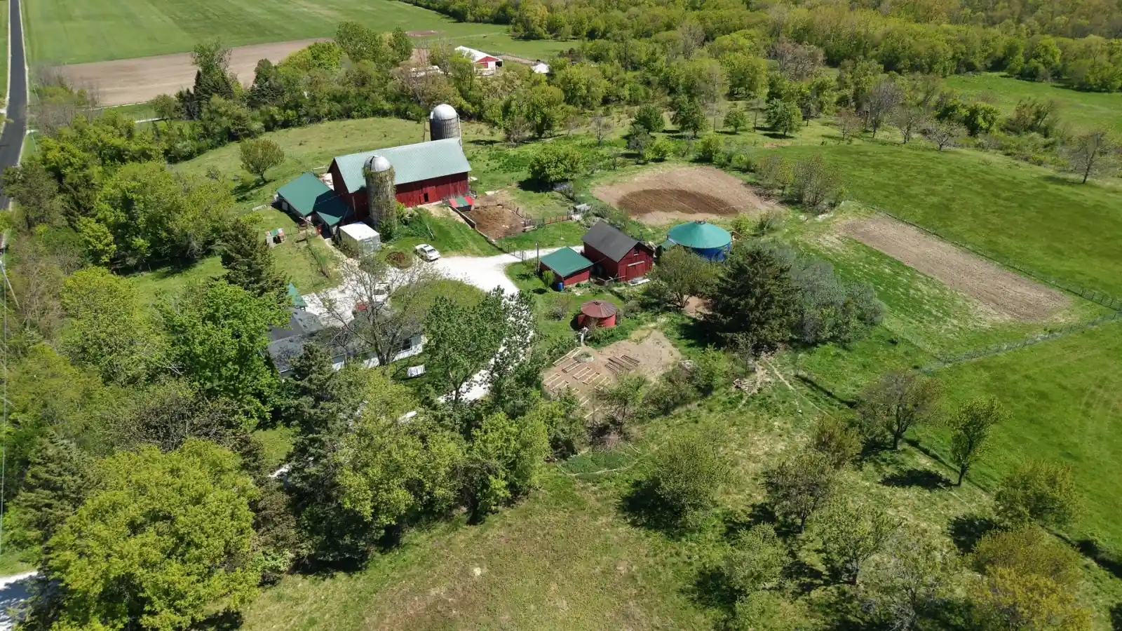 The Goldstein Farm farmstead tucked into shade trees with garden beds and outbuildings, Spring Prairie, Wisconsin